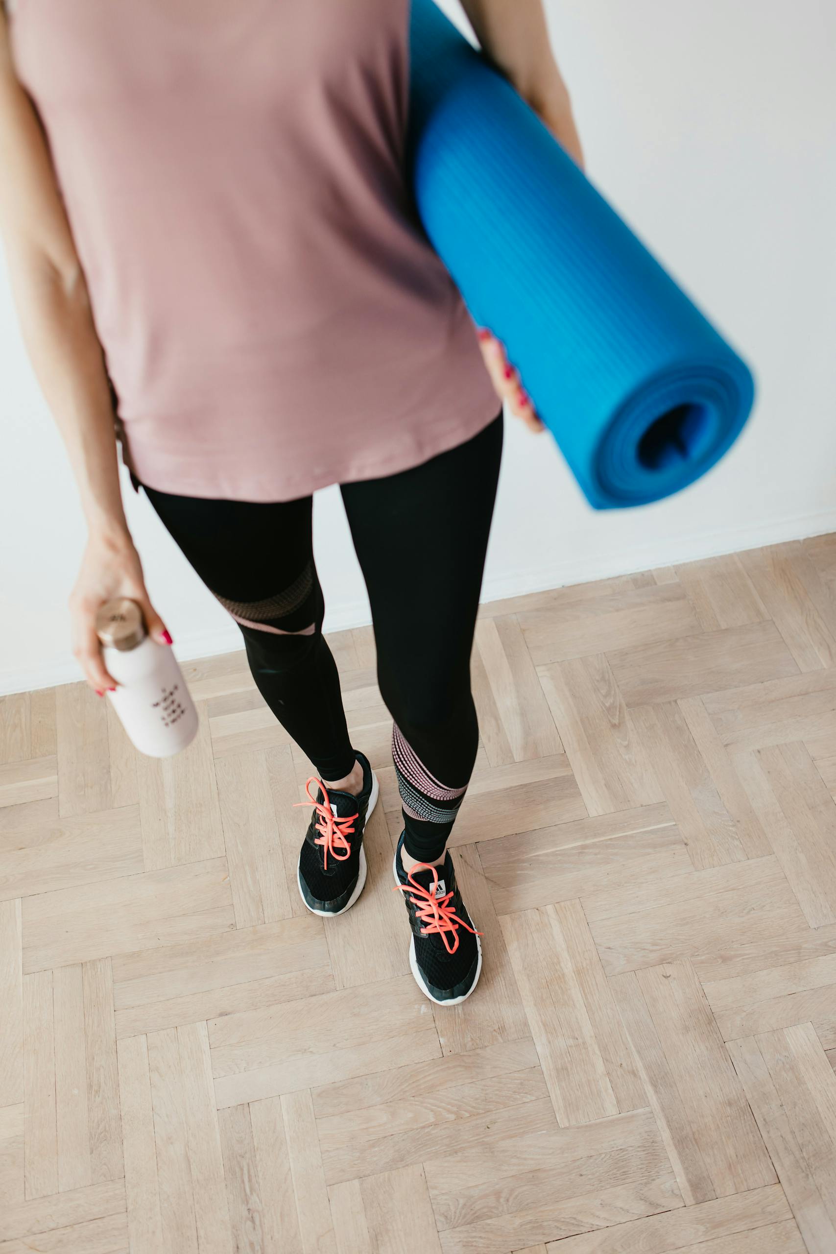 Female preparing for a yoga session indoors, holding a mat and water bottle.
